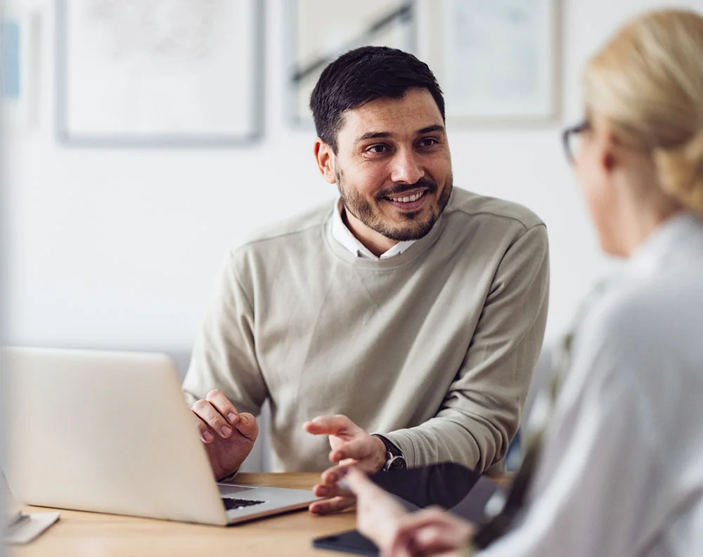 Man with his laptop talking enthusiastically to a woman