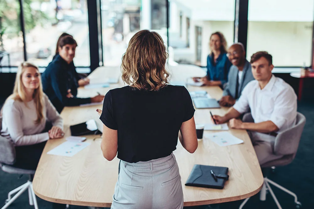 A woman at the head of a conference table giving a presentation