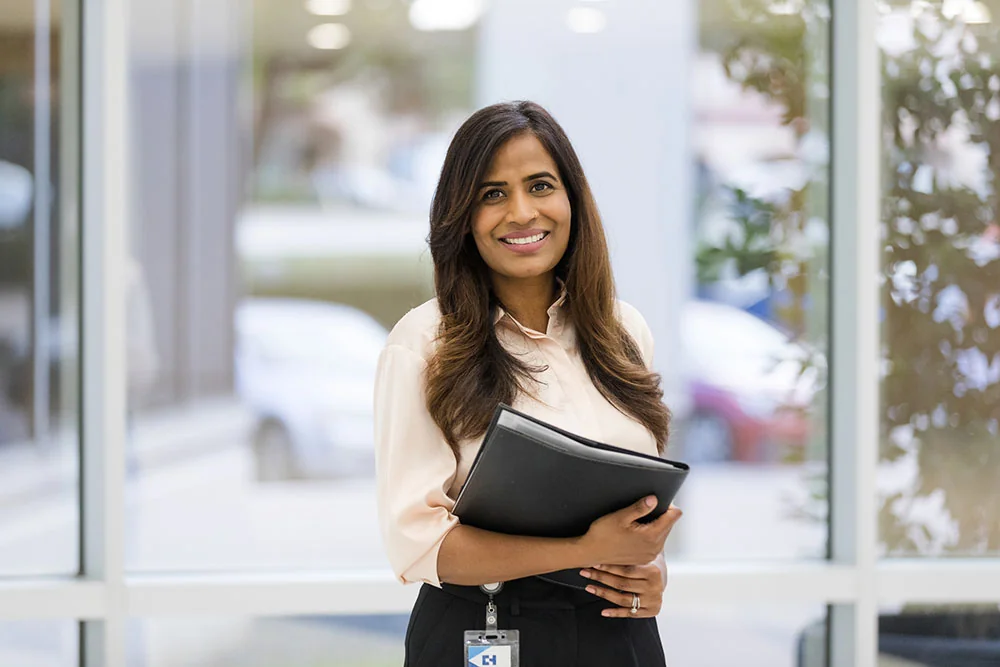 A woman wearing business clothes smiling holding a folder