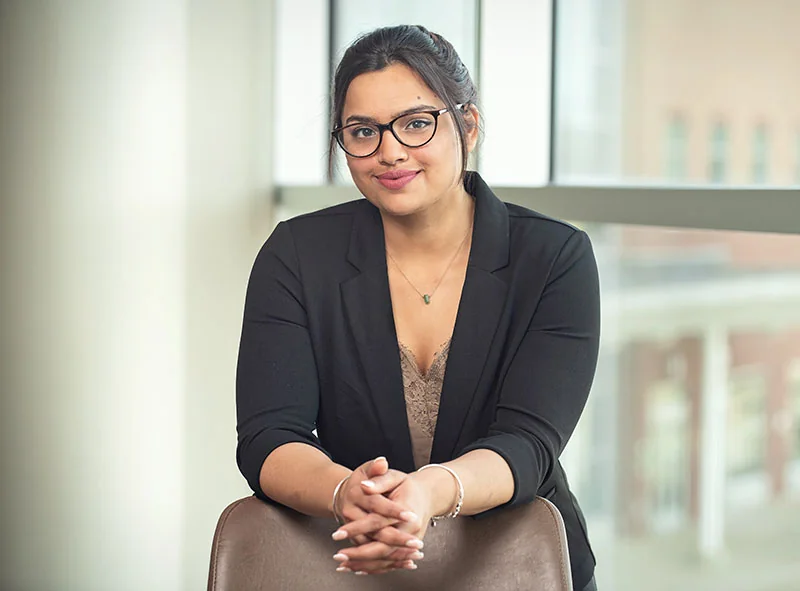A nicely dressed woman wearing glasses leaning on a chair back