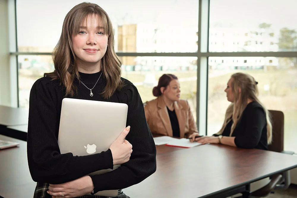 A nicely dressed woman wearing glasses leaning on a chair back