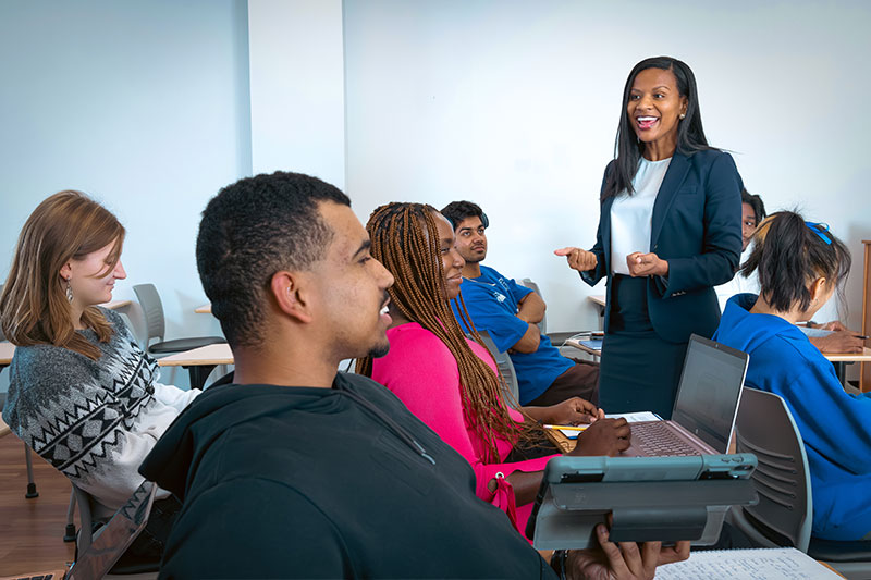 A woman in a suit smiling and speaking to students in class