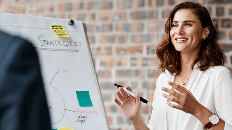 Smiling woman in a white blouse giving a presentation.