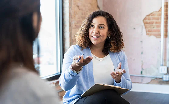 A woman in a blazer with her hand outstretched in conversation.