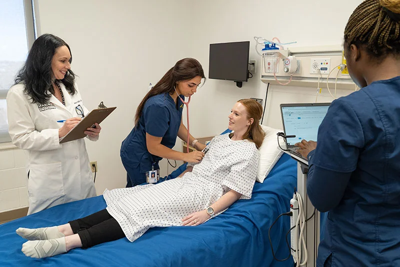 A group of smiling nurses and doctors tending to a smiling patient in a hospital.