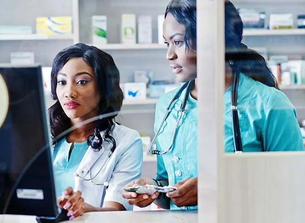 Two pharmacy professionals reviewing information on a computer in a pharmacy workspace.